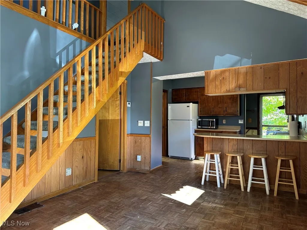 Kitchen featuring wainscoting, wooden walls, freestanding refrigerator, a high ceiling, and a kitchen bar