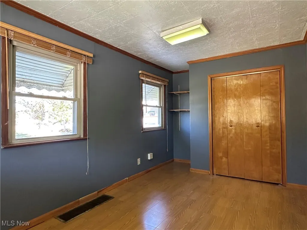 Unfurnished bedroom with ornamental molding, wood finished floors, and a closet