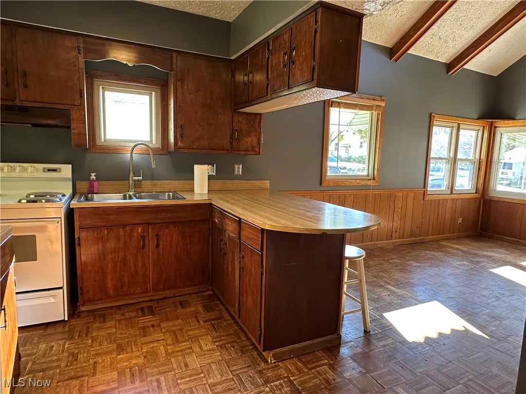 Kitchen featuring white electric range, a peninsula, wainscoting, a textured ceiling, and a kitchen breakfast bar