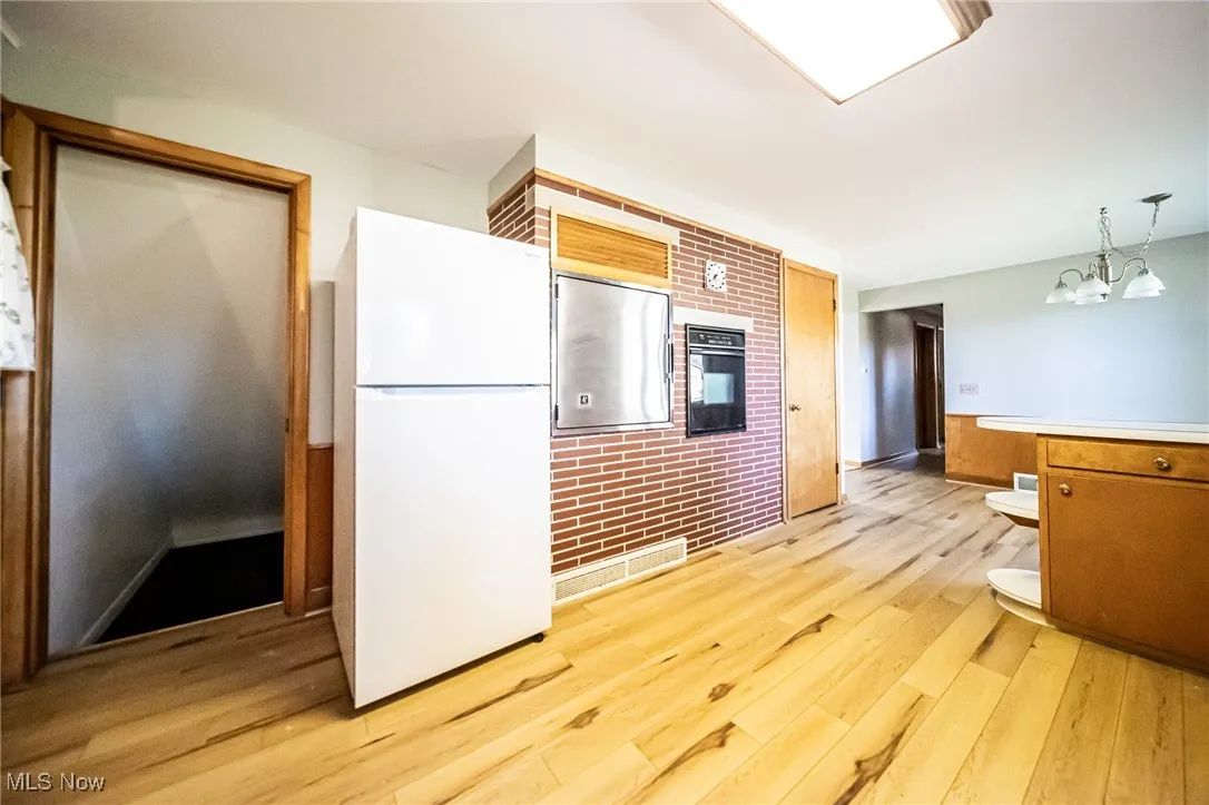 Kitchen featuring freestanding refrigerator, light countertops, light wood finished floors, oven, and hanging light fixtures