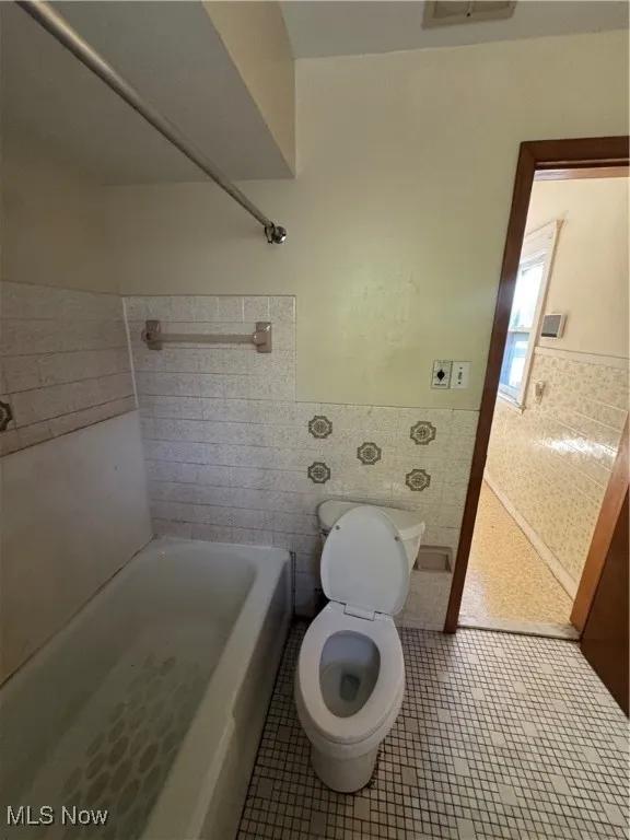 Full bathroom featuring tile patterned floors, tile walls, wainscoting, and washtub / shower combination