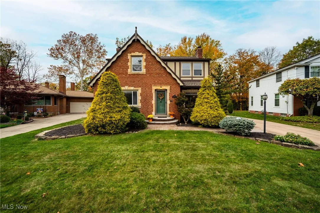 Tudor home with a front lawn, brick siding, a chimney, and concrete driveway