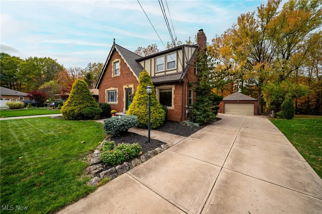 Tudor house with a front lawn, brick siding, a garage, and a chimney
