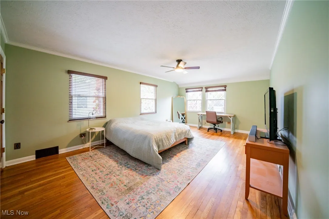 Bedroom featuring light wood-style flooring, a textured ceiling, a ceiling fan, ornamental molding, and a desk