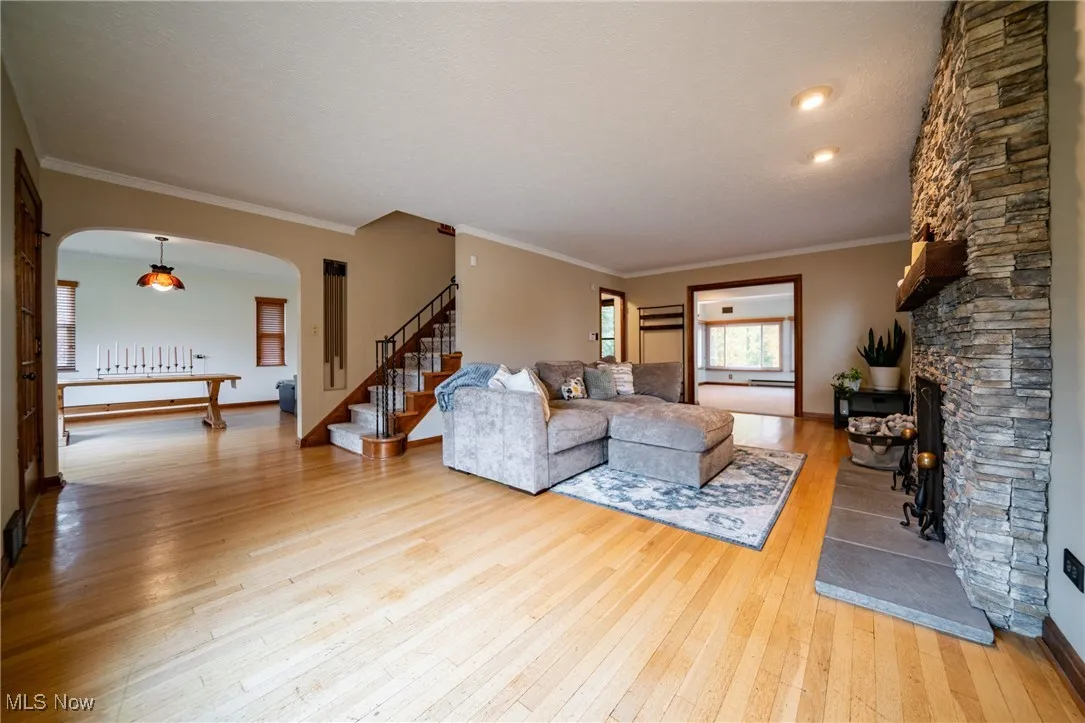 Living area featuring ornamental molding, light wood-style floors, arched walkways, stairs, and a fireplace