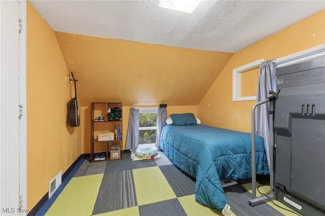 Bedroom with vaulted ceiling, carpet flooring, and a textured ceiling