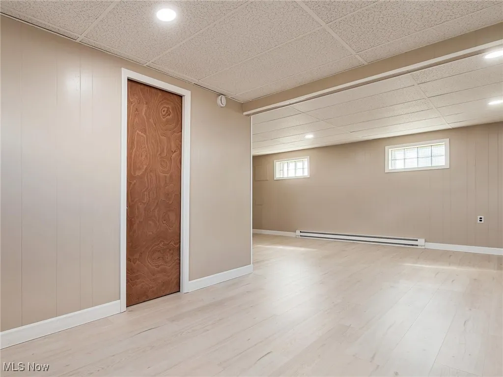 Basement featuring a paneled ceiling, wood walls, light wood-type flooring, baseboard heating, and recessed lighting