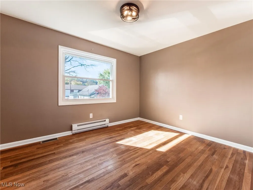 Empty room with a baseboard heating unit and wood finished floors