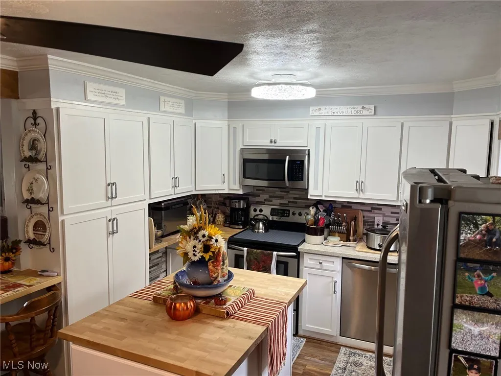Kitchen with white cabinetry, butcher block counters, a textured ceiling, stainless steel appliances, and crown molding