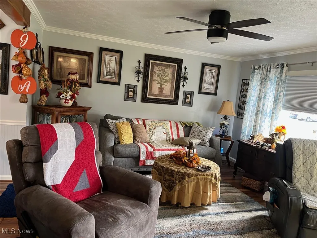 Living room featuring a textured ceiling, crown molding, laminate flooring and a ceiling fan