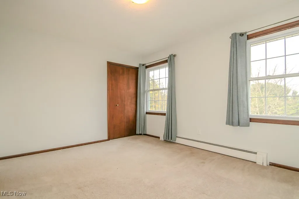 Unfurnished room with baseboard heating and light colored carpet