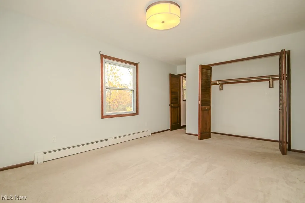 Unfurnished bedroom with a baseboard heating unit, a closet, and light carpet