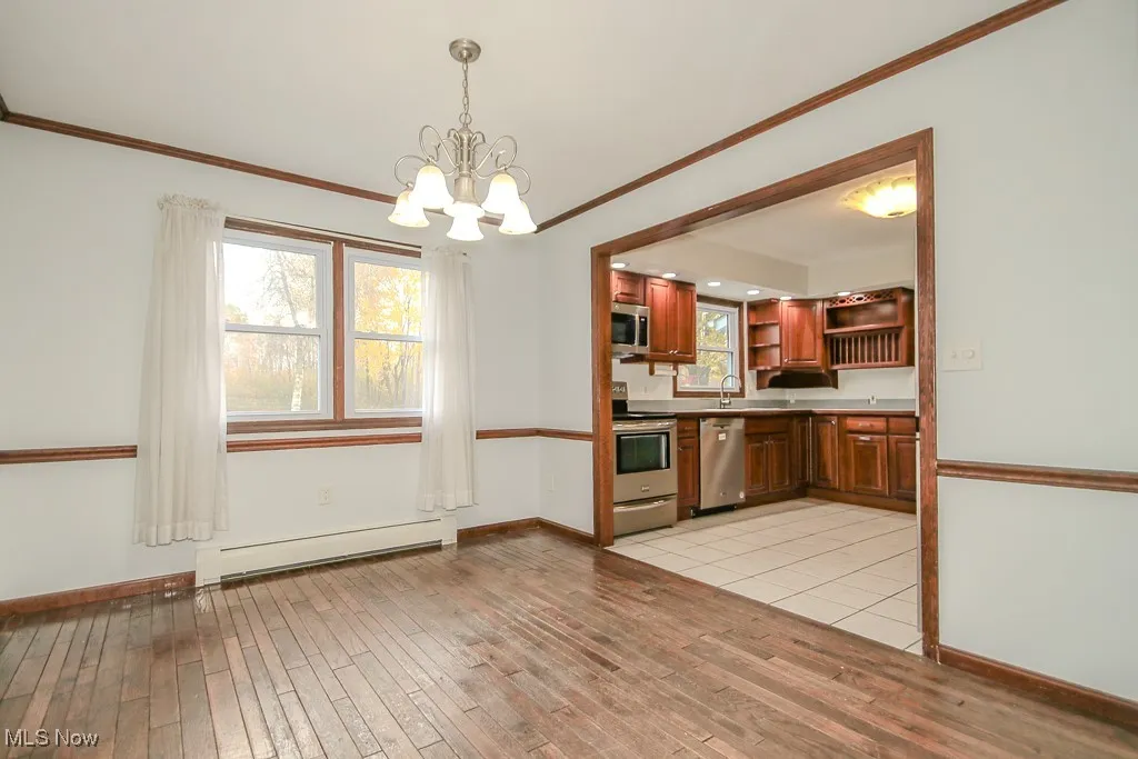 Kitchen featuring appliances with stainless steel finishes, a baseboard radiator, crown molding, pendant lighting, and a chandelier