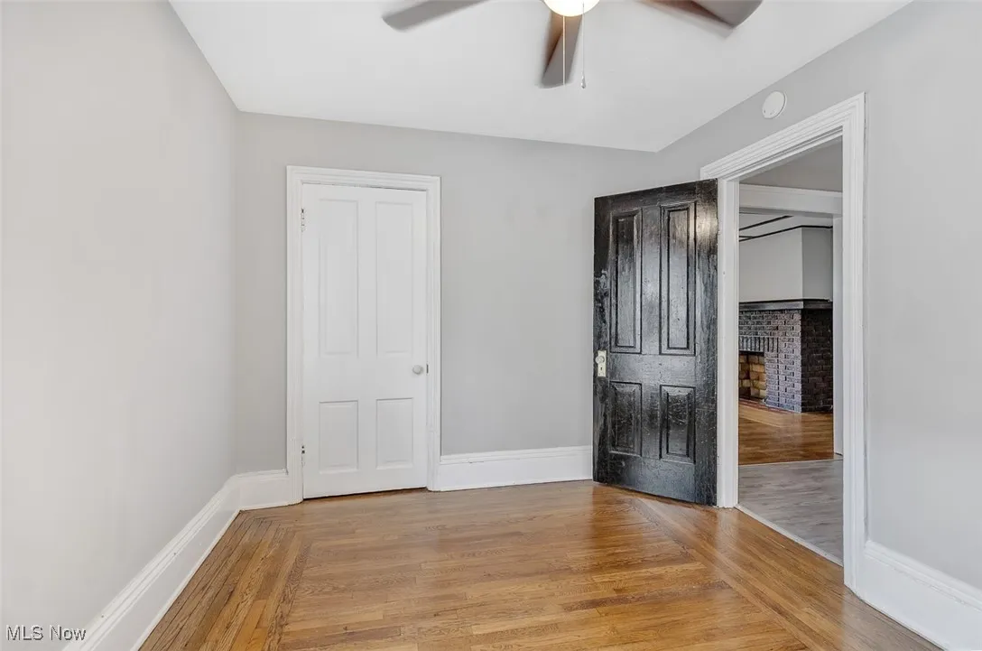 Unfurnished bedroom featuring light wood-style flooring, a ceiling fan, and a brick fireplace