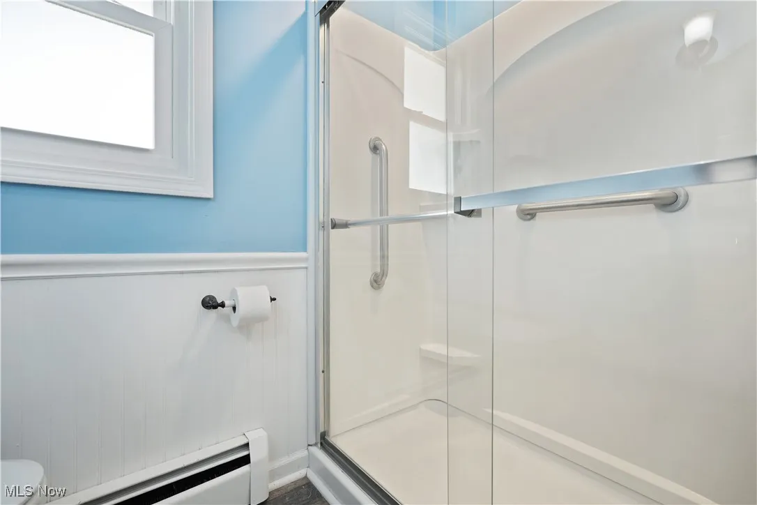 Full bathroom featuring a baseboard heating unit, a shower stall, and wainscoting