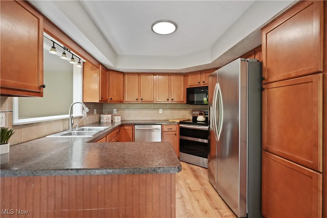 Kitchen featuring appliances with stainless steel finishes, backsplash, light wood finished floors, brown cabinets, and a peninsula