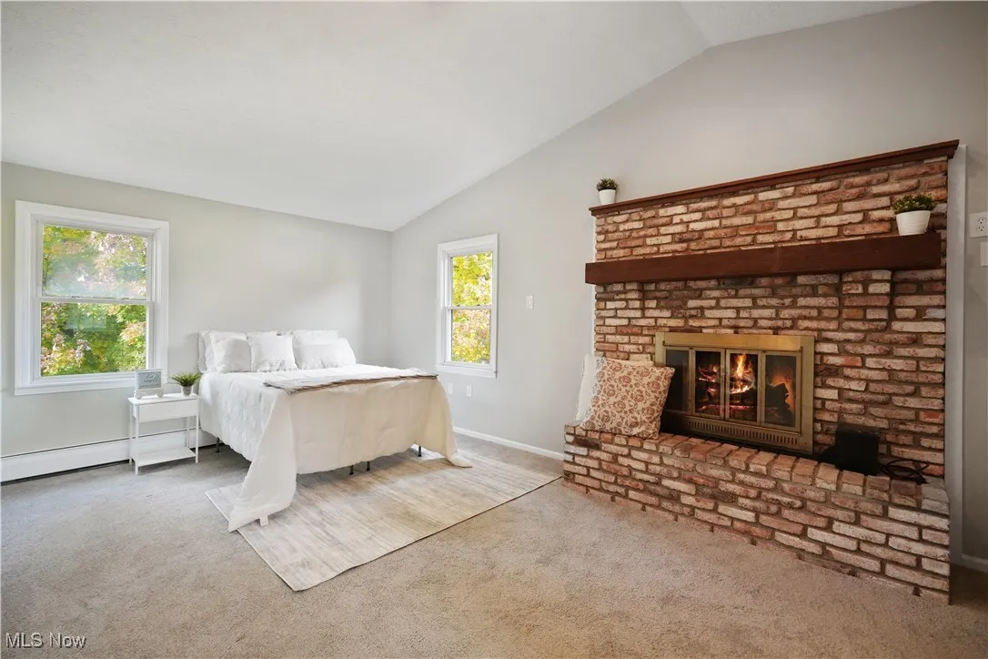 Bedroom featuring vaulted ceiling, carpet flooring, a fireplace, and baseboard heating