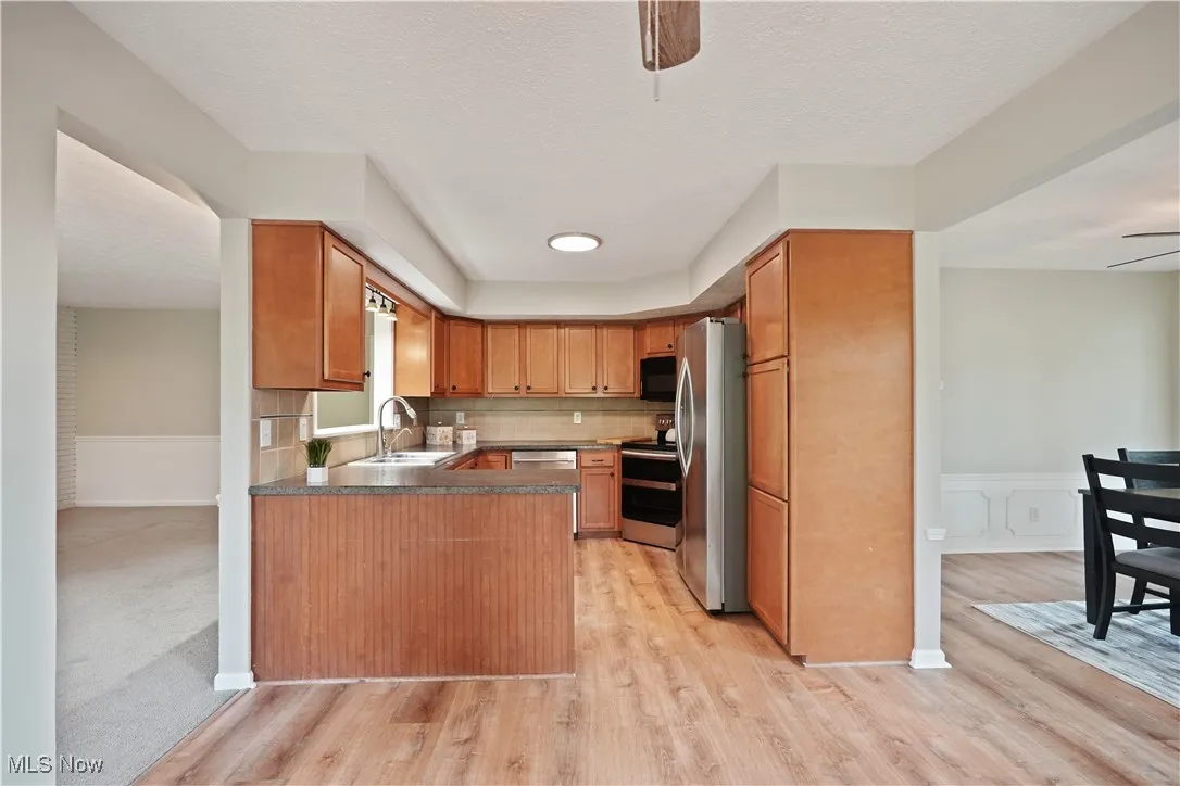 Kitchen with a ceiling fan, a wainscoted wall, brown cabinets, appliances with stainless steel finishes, and a textured ceiling