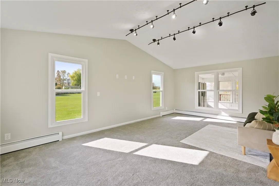 Spare room with vaulted ceiling, a baseboard radiator, carpet flooring, plenty of natural light, and track lighting
