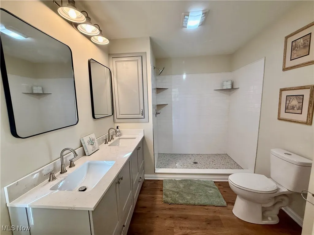 Full bathroom featuring double vanity, walk in shower, and dark wood-style floors