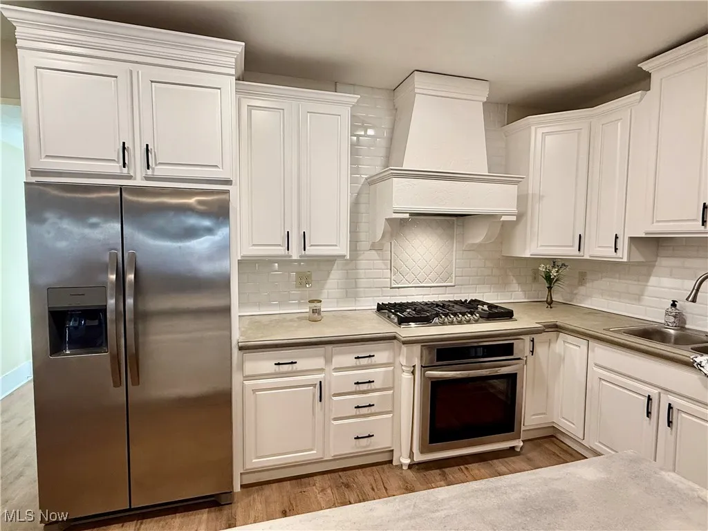 Kitchen featuring appliances with stainless steel finishes, light countertops, backsplash, and white cabinetry