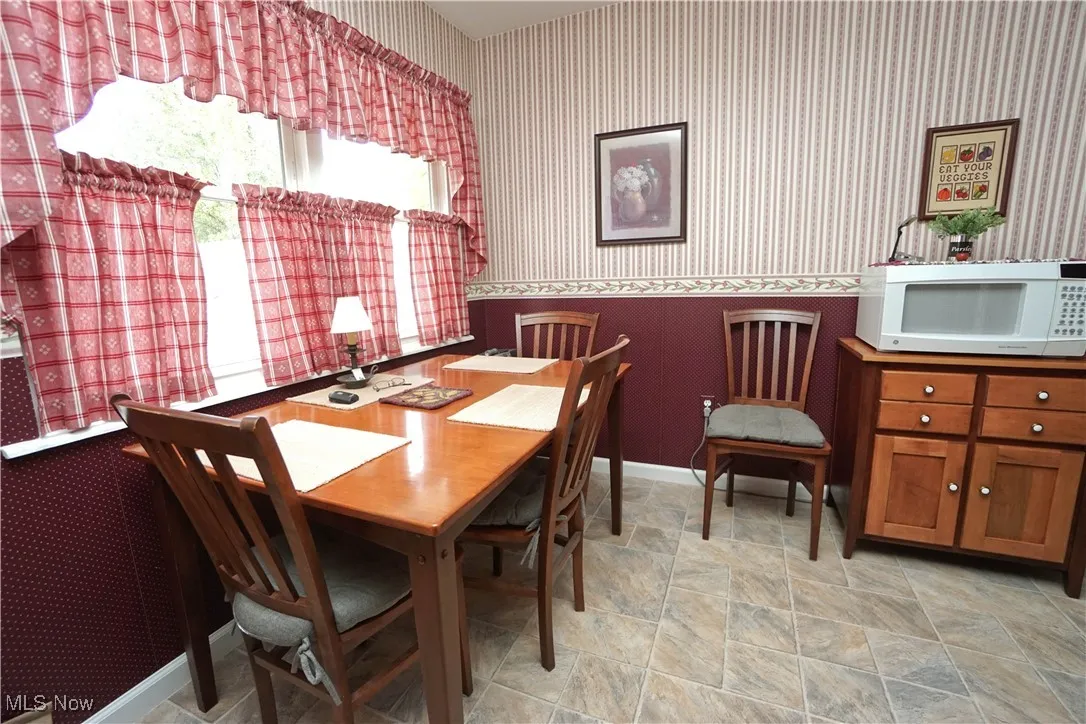 Dining space featuring wallpapered walls, a wainscoted wall, and stone finish floors