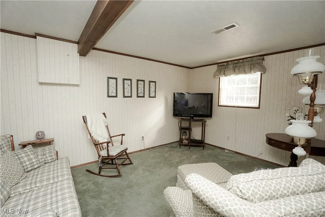 Living area with carpet, crown molding, and beamed ceiling