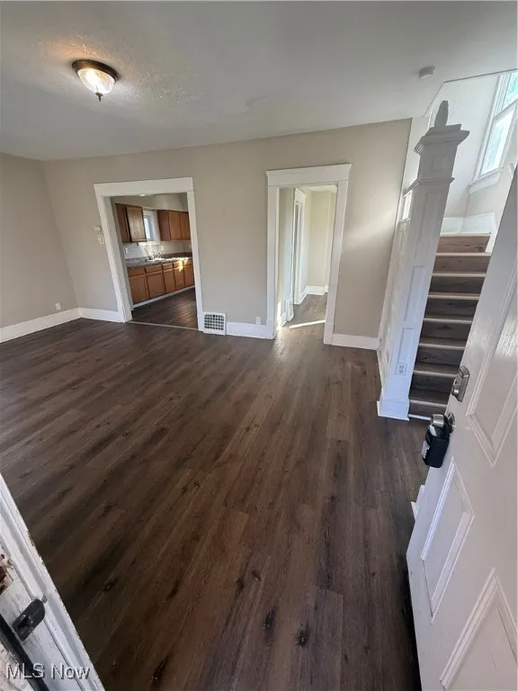Unfurnished living room featuring dark wood-style floors, stairway, and a textured ceiling
