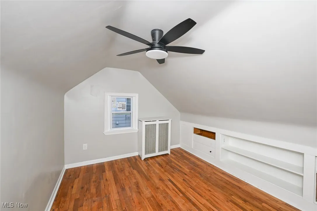 Bonus room featuring built in shelves, dark wood finished floors, and lofted ceiling