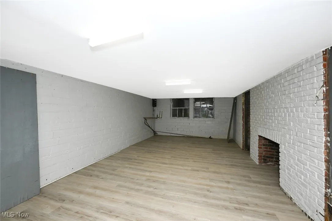 Finished basement with light wood-type flooring and a brick fireplace