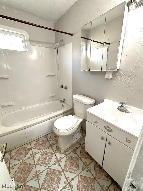 Full bathroom with a textured wall, vanity, and  shower combination