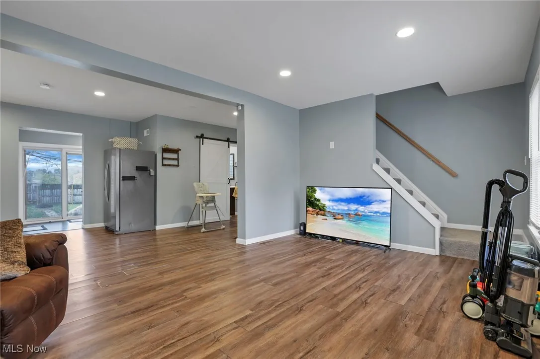 Living area with a barn door, wood finished floors, recessed lighting, and stairs