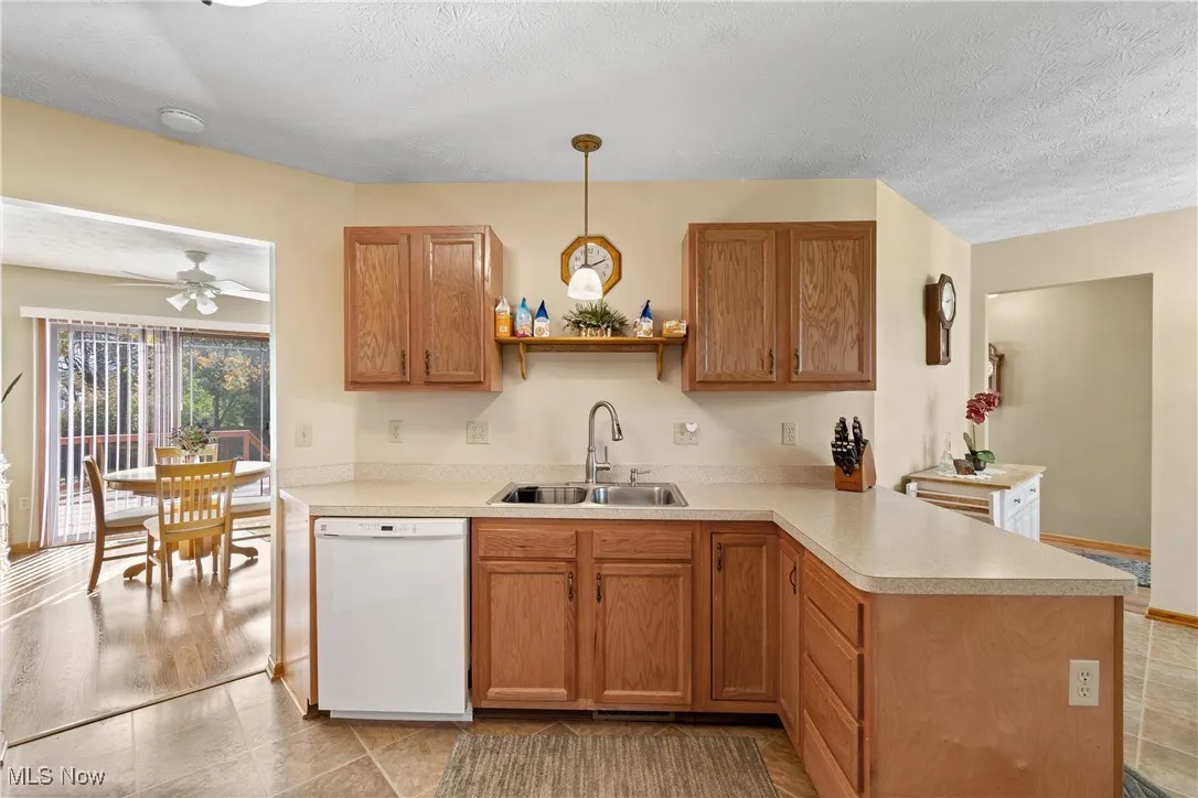 Kitchen featuring white dishwasher, light countertops, brown cabinetry, a textured ceiling, and decorative light fixtures