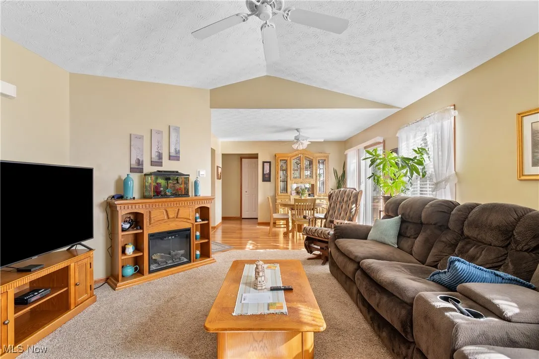 Living area featuring vaulted ceiling, light colored carpet, a textured ceiling, and a glass covered fireplace