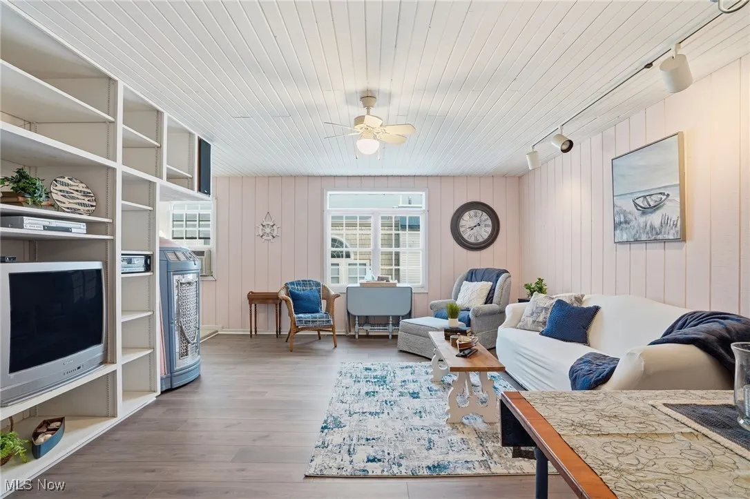Living area with light wood-style flooring, a ceiling fan, wood walls, and rail lighting