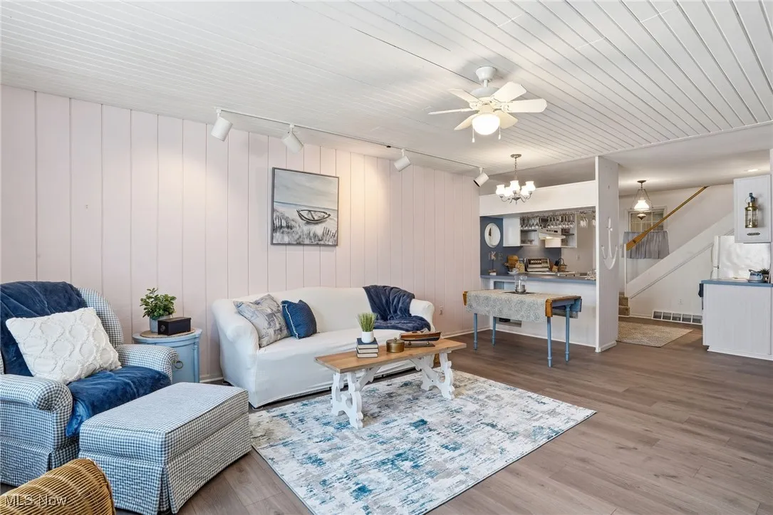 Living room with wood finished floors, a ceiling fan, stairs, track lighting, and wooden walls