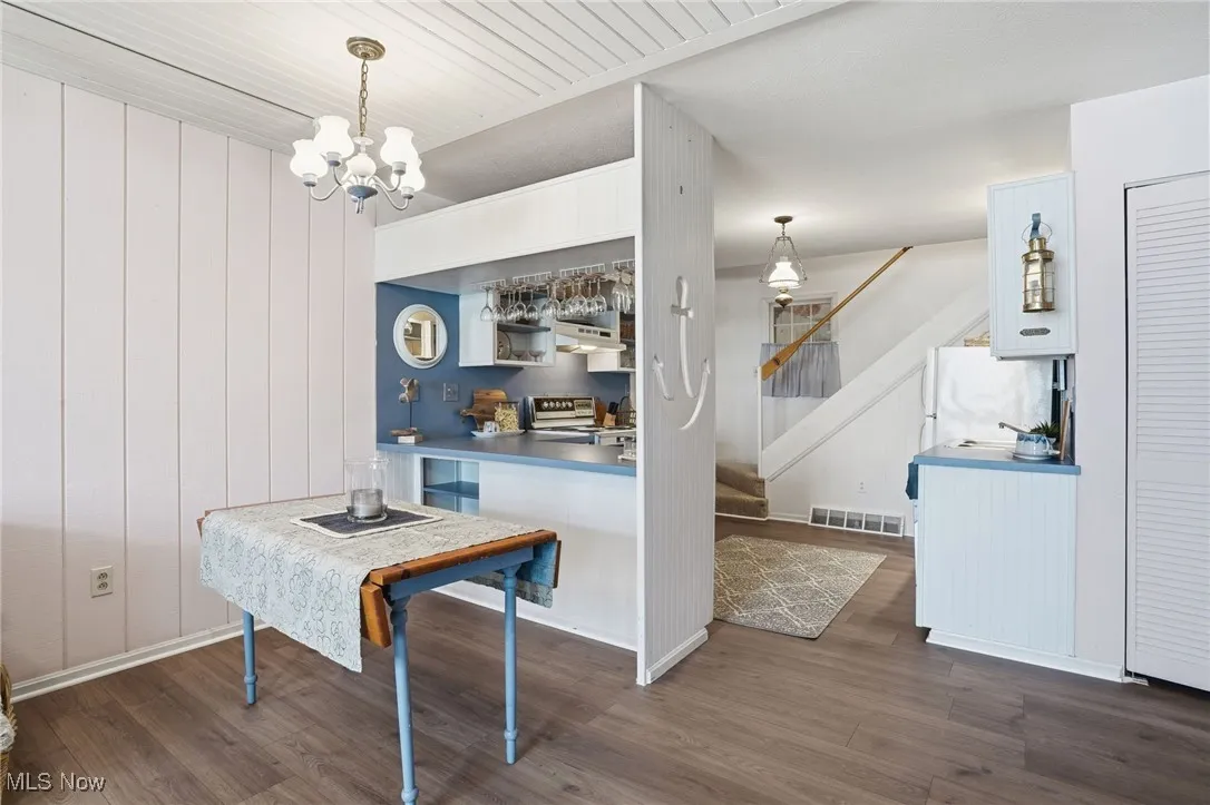 Dining area featuring dark wood-style floors, a chandelier, stairway, and wood walls