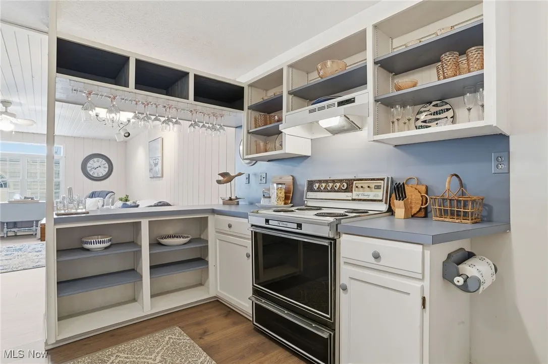 Kitchen with open shelves, electric range, white cabinetry, under cabinet range hood, and dark wood-type flooring