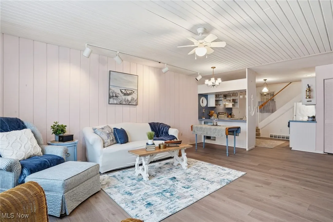 Living area featuring stairway, wood finished floors, rail lighting, a ceiling fan, and wood walls