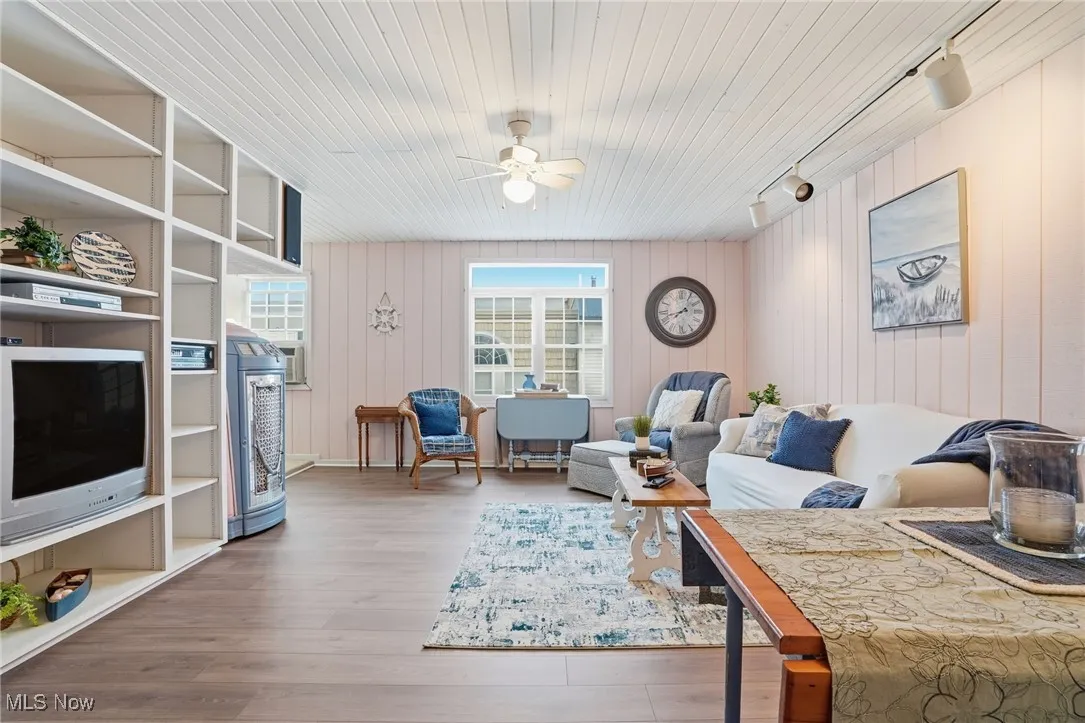 Living area with track lighting, light wood-style floors, a ceiling fan, and wood walls