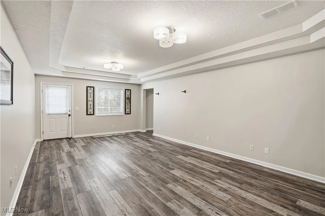 Unfurnished room with a tray ceiling, a textured ceiling, and dark wood-style flooring