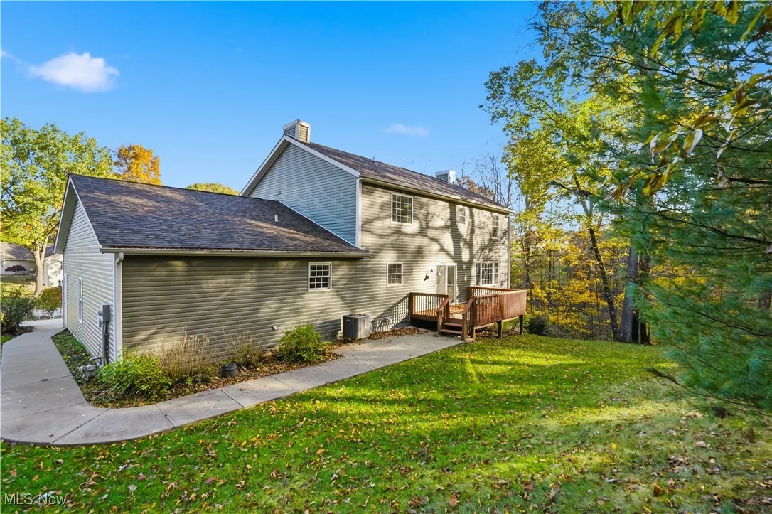 Back of house featuring a chimney, a lawn, a wooden deck, and roof with shingles
