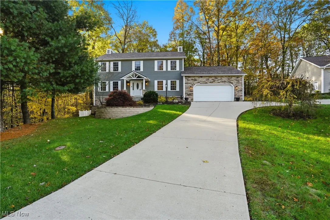 Colonial inspired home with a chimney, a front lawn, concrete driveway, stone siding, and a garage