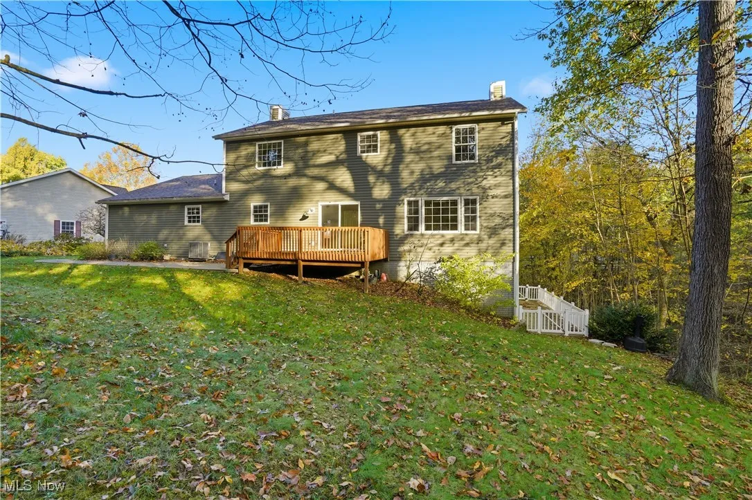 Back of house featuring a chimney, a lawn, and a wooden deck