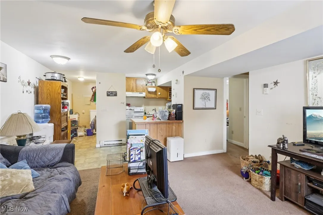 Living room with ceiling fan, light colored carpet, and baseboard heating