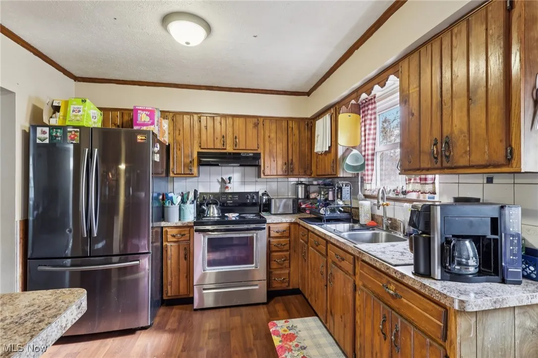 Kitchen with appliances with stainless steel finishes, decorative backsplash, light countertops, crown molding, and dark wood-style flooring