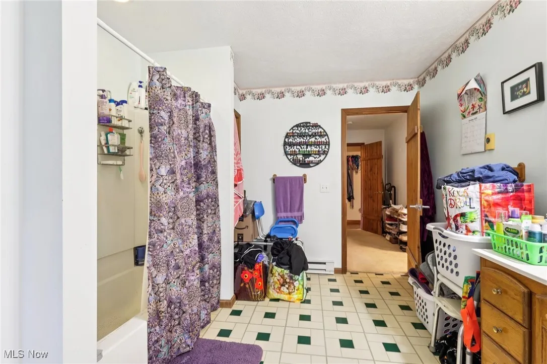 Full bath featuring shower / tub combo and a baseboard heating unit