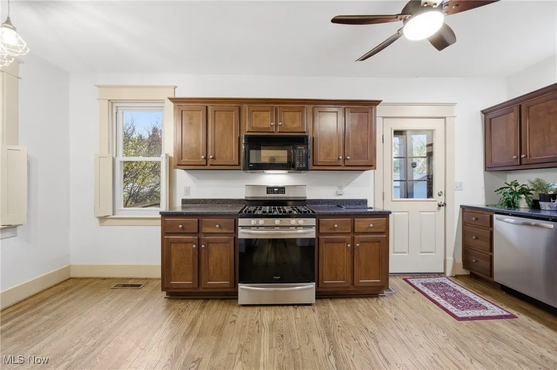 Kitchen with appliances with stainless steel finishes, light wood finished floors, pendant lighting, and dark stone countertops