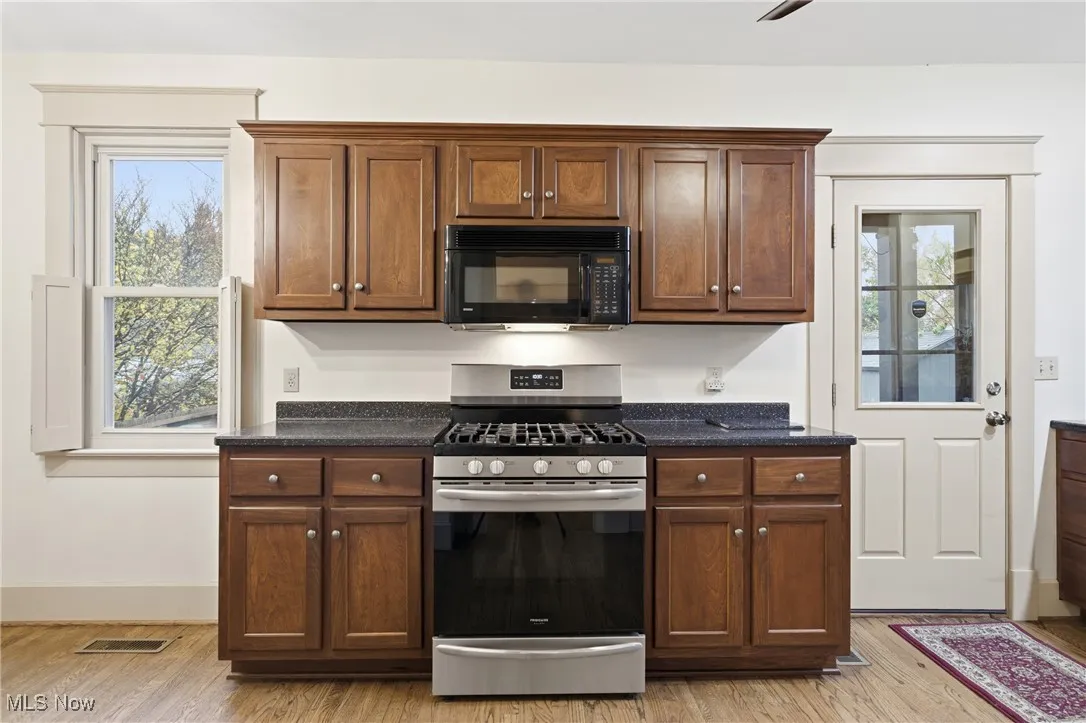 Kitchen with gas stove, black microwave, light wood finished floors, and ceiling fan