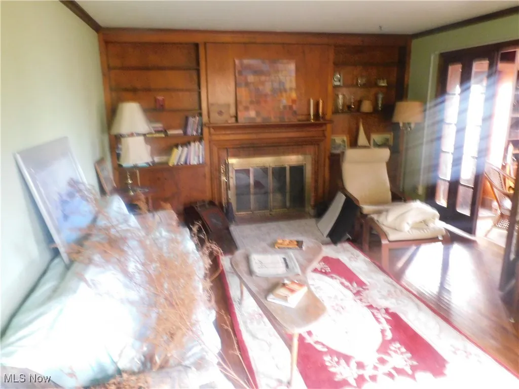 Living room view b area with a glass covered fireplace, built in features, ornamental molding, and wood finished floors